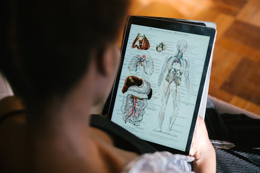 A woman studies anatomy diagrams on a tablet indoors, focusing on educational material.